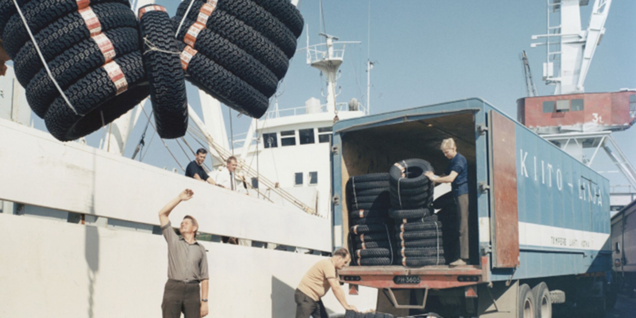 Men loading tires from a vehicle onto a ship at the docks.