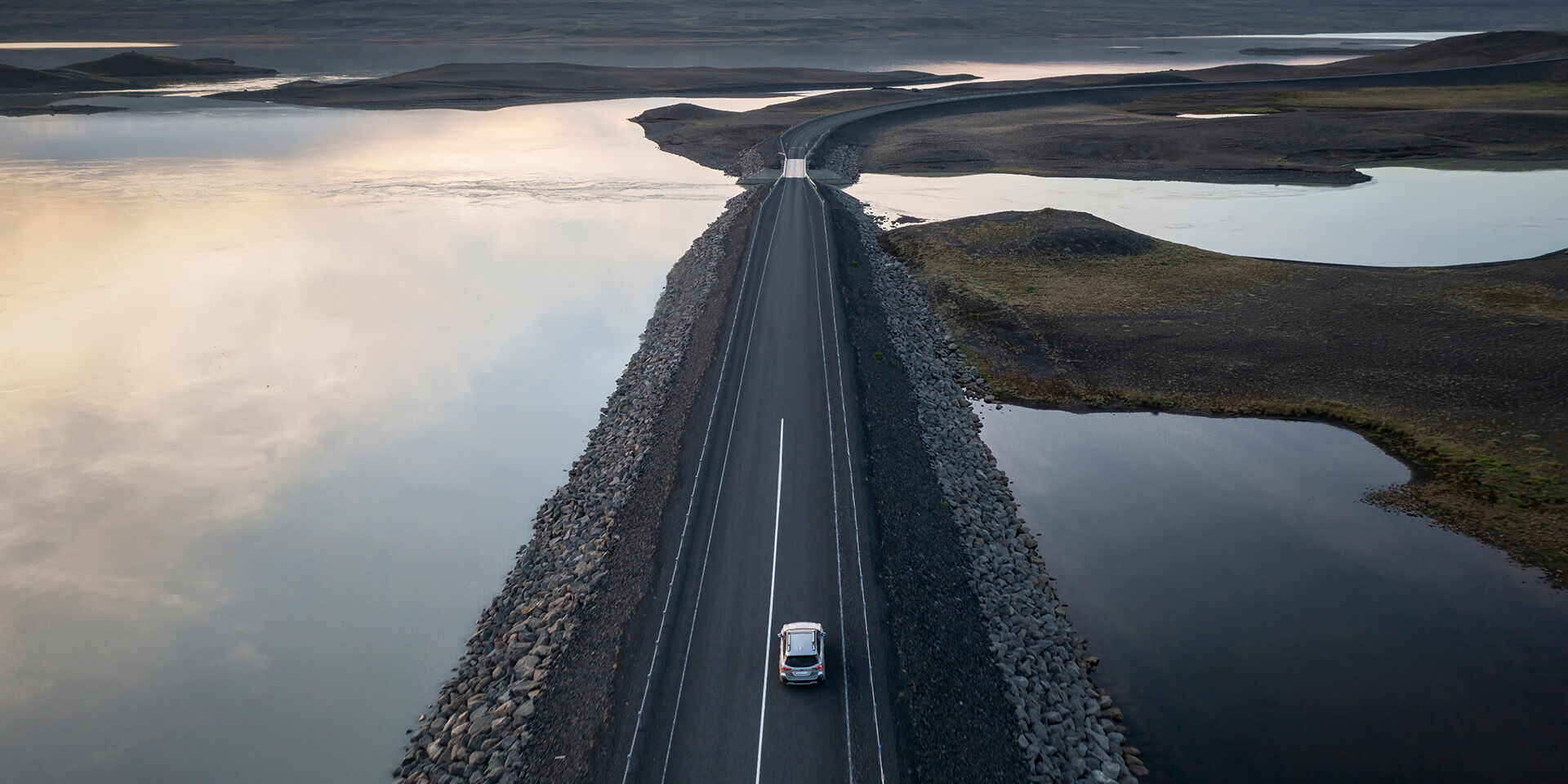 Aerial view of car driving by water on asphalt road