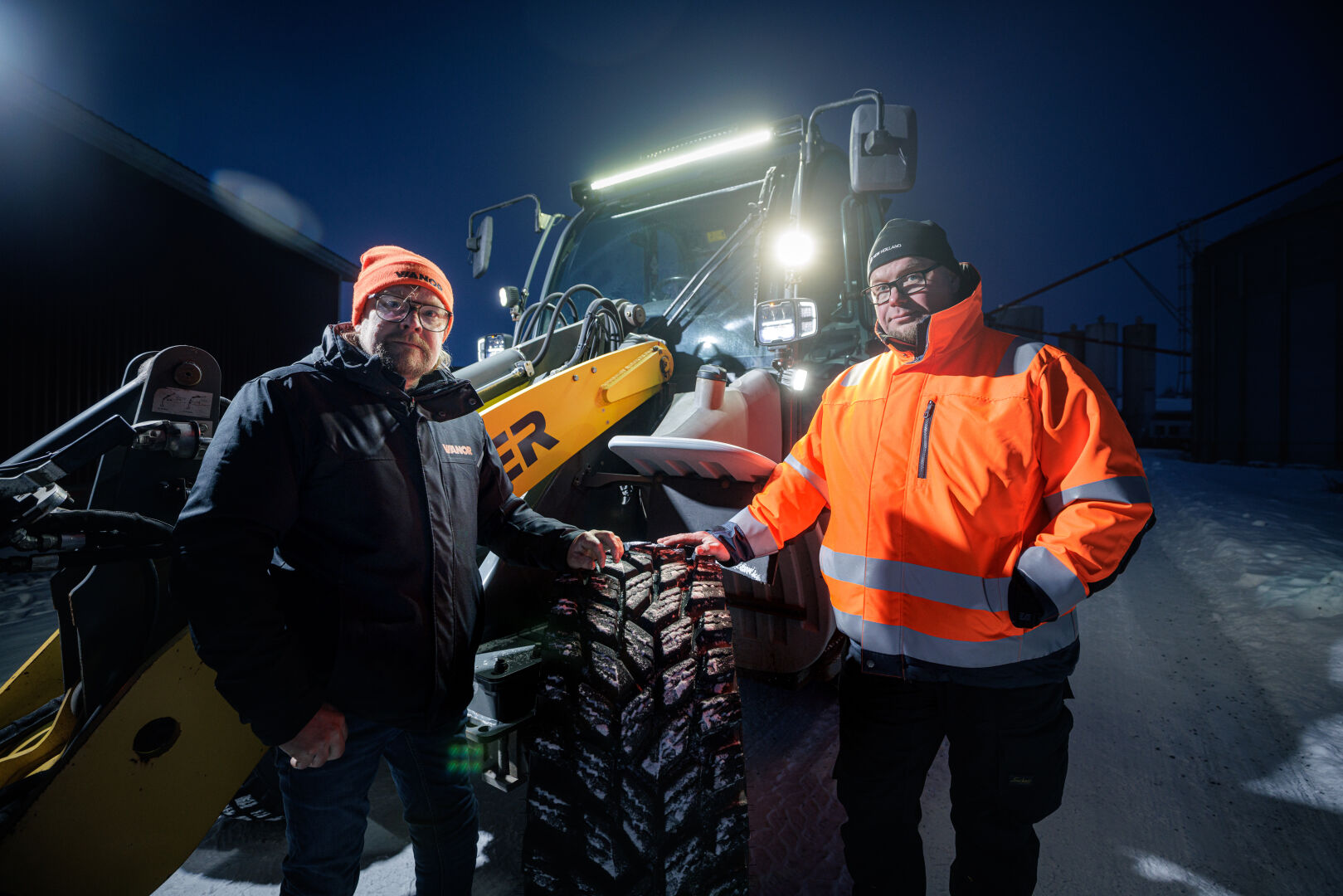 Kaksi miestä seisoo traktorin edessä, jossa on Nokian Tyres Hakkapeliitta TRI -renkaat, lumisessa ympäristössä.