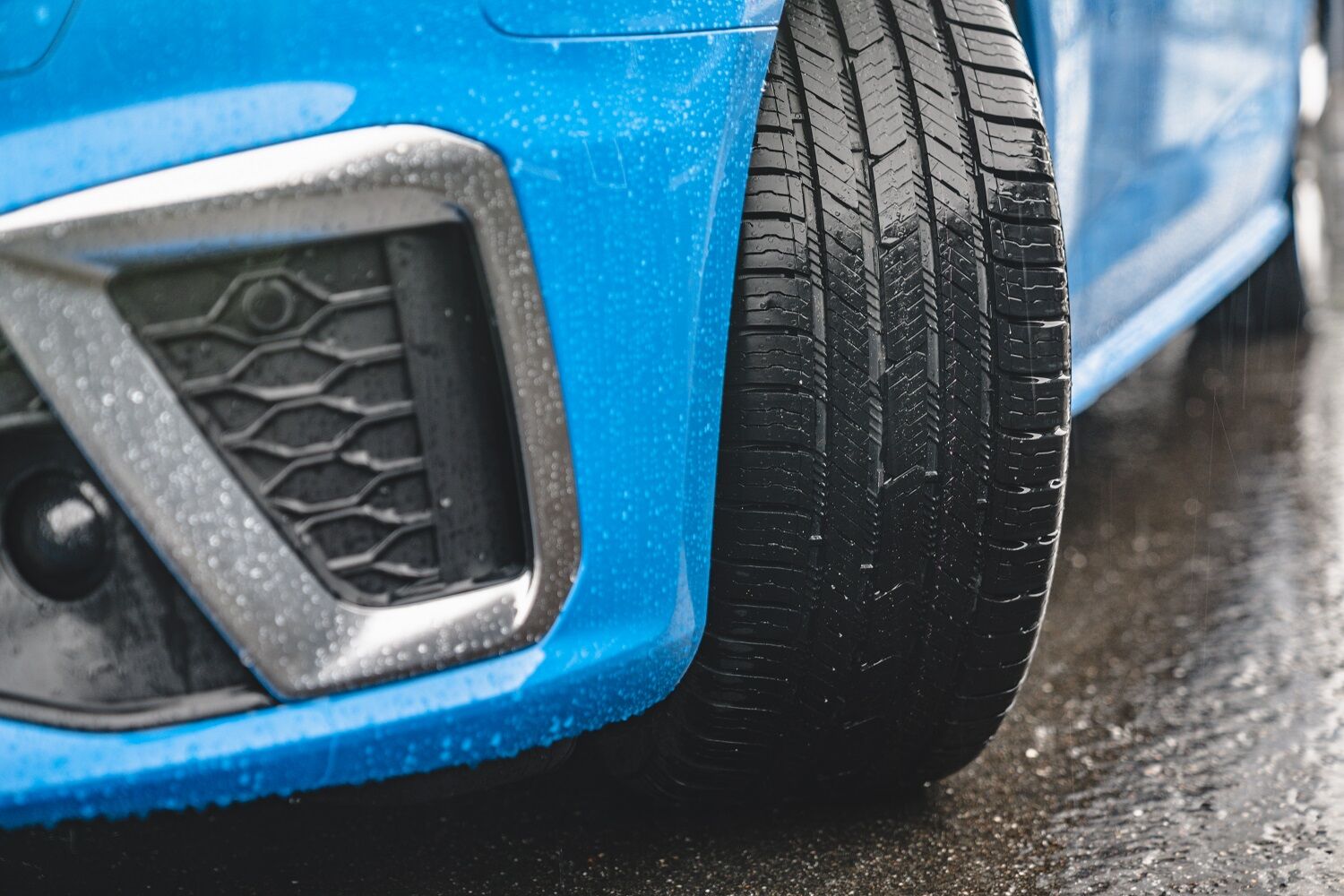 Close up of Nokian Tyres One tread on front panel of blue passenger car in rainy conditions